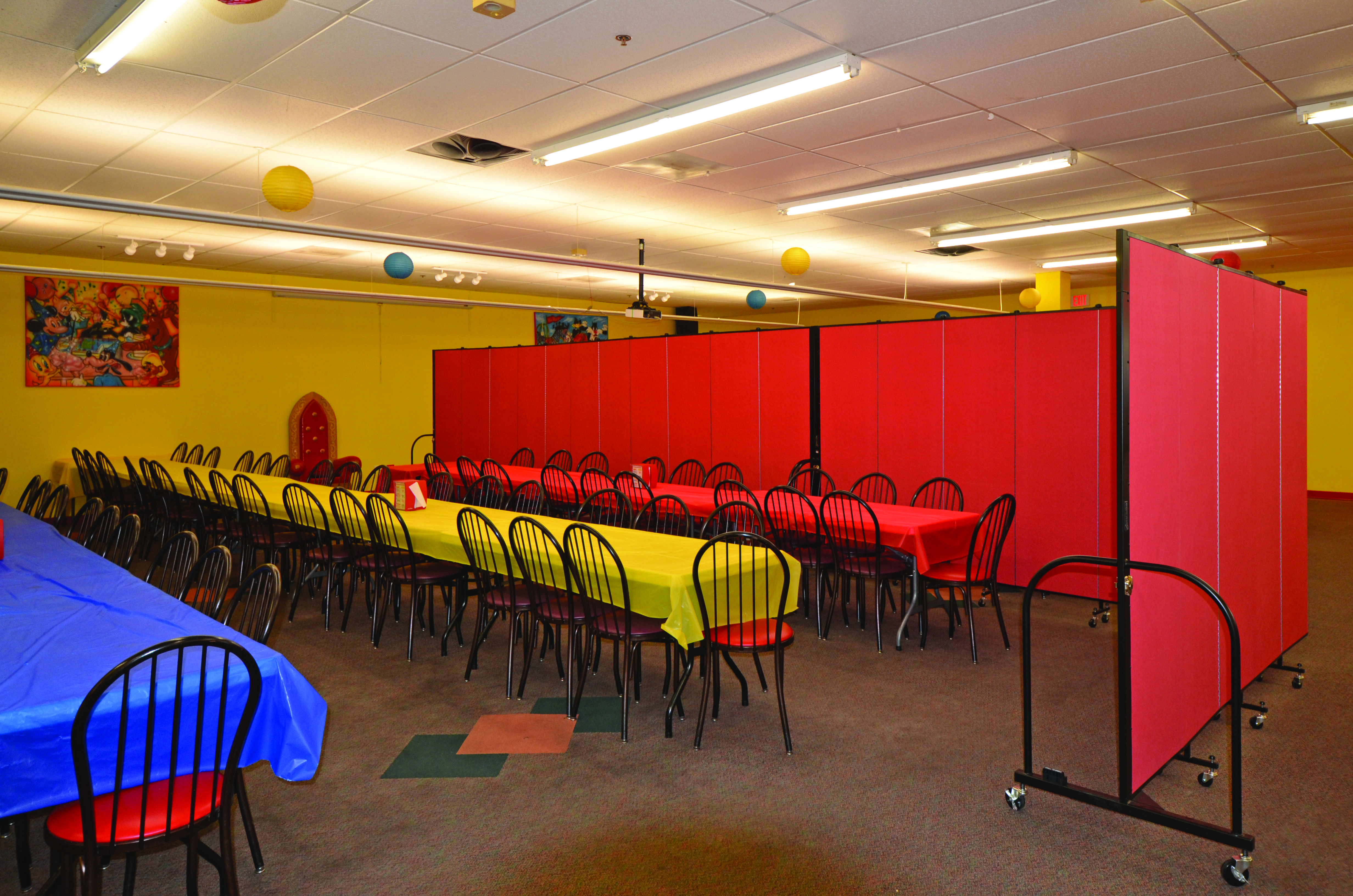 A colorful party room is divided into two eating areas with a red Screenflex Room Divider.