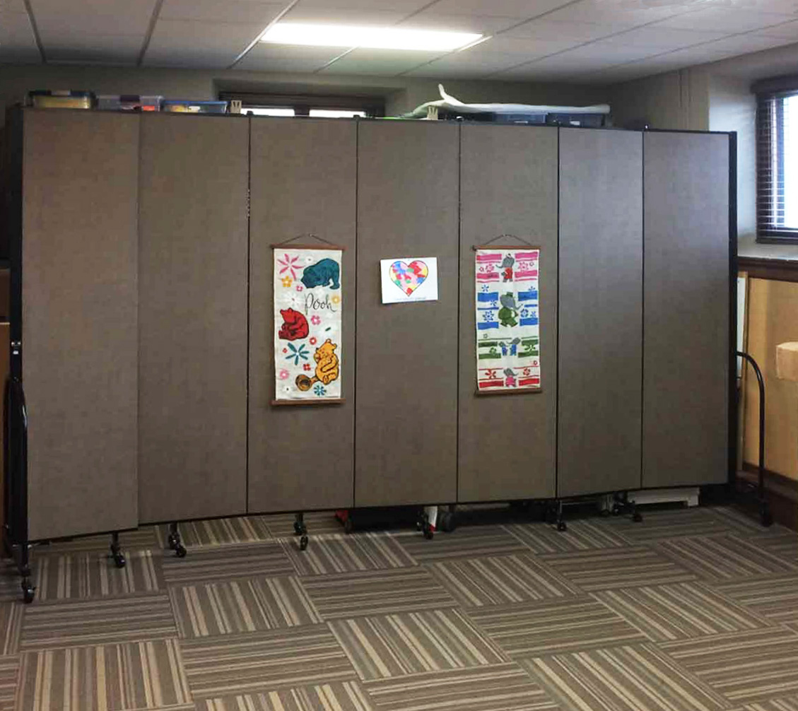 Posters are tacked to a 7-panel Screenflex folding wall partition that is opened in a classroom