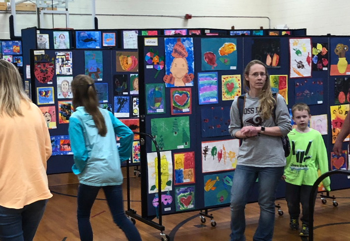 People look at student artwork attached to black display walls