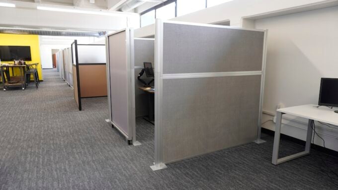 Row of partitioned cubicles in an open-plan office with carpeted floors and desks.