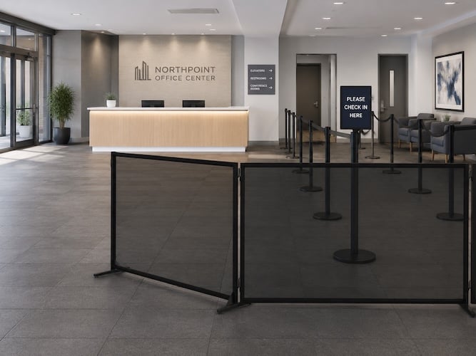Office reception area with modular black crowd-control barriers guiding visitors toward a check-in desk in a modern lobby.