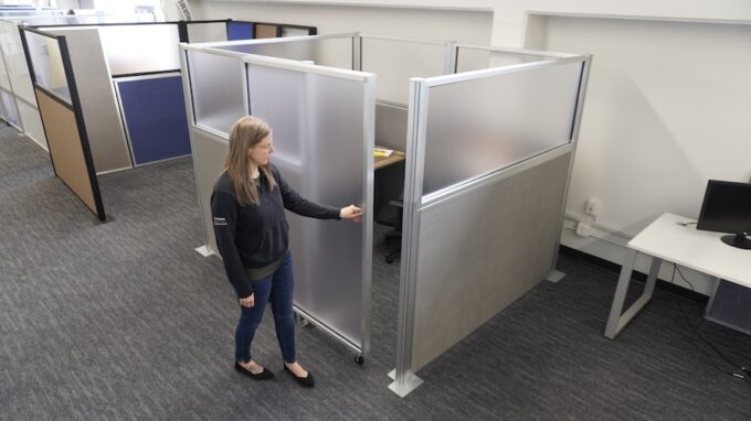 Office cubicle setup with gray and frosted panels, showing a person adjust a sliding door panel in a modern workspace.
