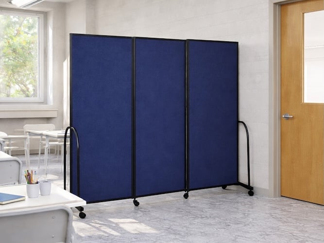 Blue freestanding folding security partition on casters positioned inside a bright classroom near desks, chairs, and a wooden door.